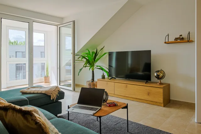 Wohnzimmer mit Fernseher, Holzsideboard und verglastem Zugang zum Wintergarten.