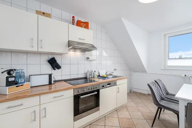 Küchenzeile unter der Dachschräge mit Fenster und grauen Essstühlen.
