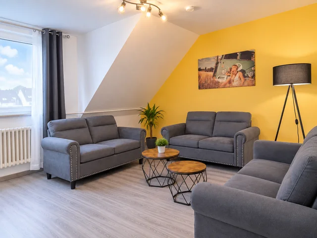 Wohnzimmer mit grauen Sofas vor einer gelben Wand und Fenster unter der Dachschräge.