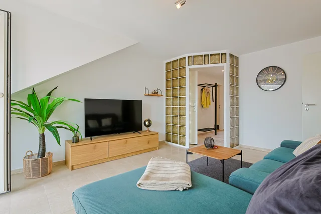 Wohnzimmer mit Ecksofa, Fernseher und angrenzendem Flur.